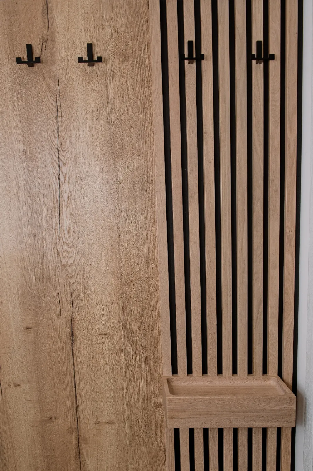 Dubový věšákový panel s odkládací miskou Detail dubové předsíňové stěny s lamelovým panelem, věšákovými háčky a odkládací miskou.